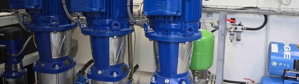 Vier blaue vertikale Pumpen in einer technischen Anlage mit grünem Druckbehälter und Steuerungseinheit an der Wand