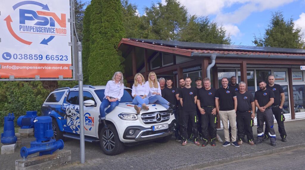 Team von Pumpenservice Nord steht vor Firmengebäude und weißem Mercedes-Benz mit Firmenlogo, drei Frauen sitzen auf der Motorhaube