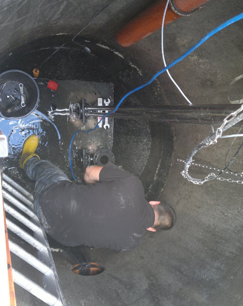 Person in schwarzer Kleidung arbeitet in einem engen Schacht mit technischen Geräten und blauen Kabeln