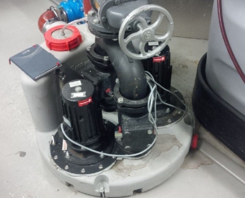 Abwasserhebeanlage mit zwei schwarzen Elektromotoren, grauem Rohrsystem und Handrad auf rundem Sockel