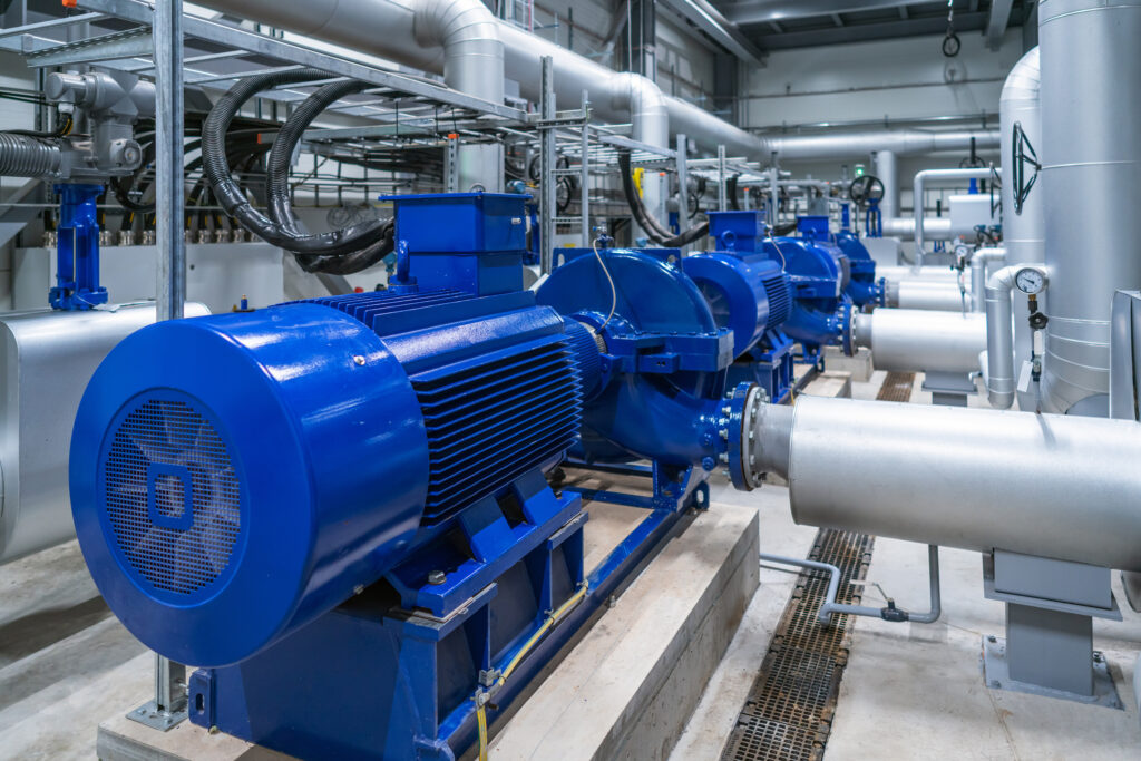 Reihe von blauen Industriemotoren mit angeschlossenen großen silbernen Rohrleitungen in einer technischen Anlage