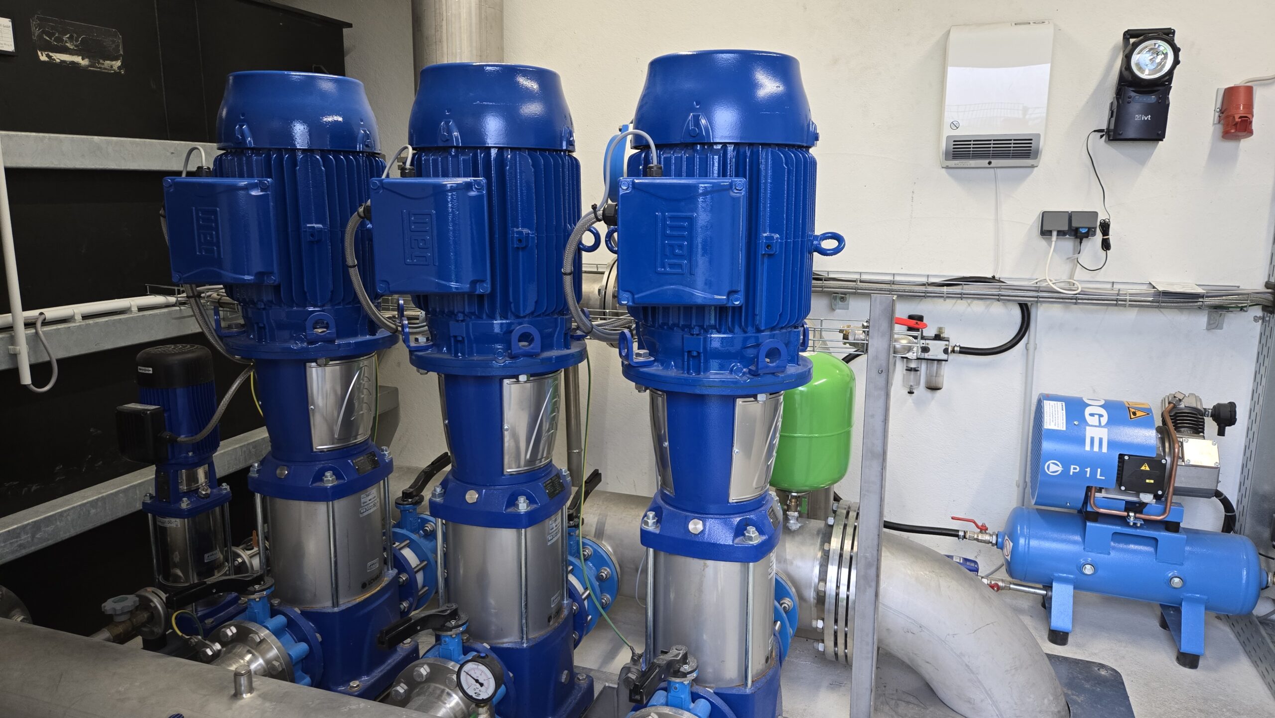 Druckerhöhungsanlage mit drei blauen Elektromotoren und Pumpen in einem Technikraum