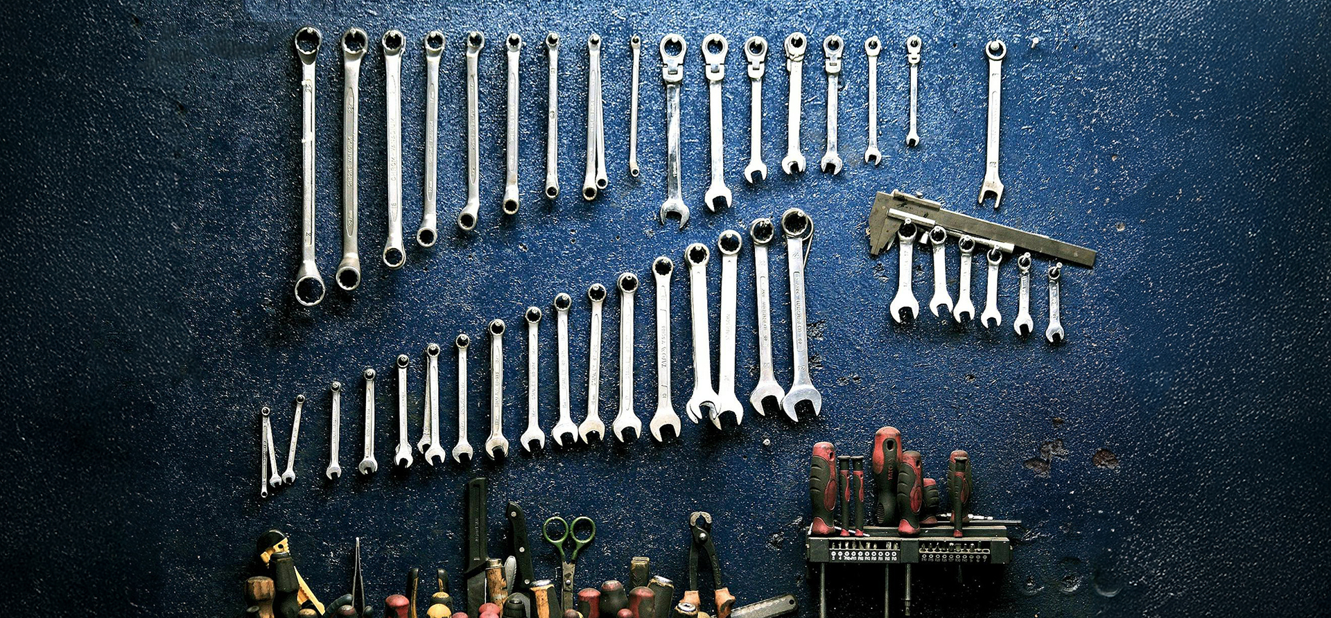 Werkzeugwand mit verschiedenen Schraubenschlüsseln und Schraubendrehern an einer blauen Wand