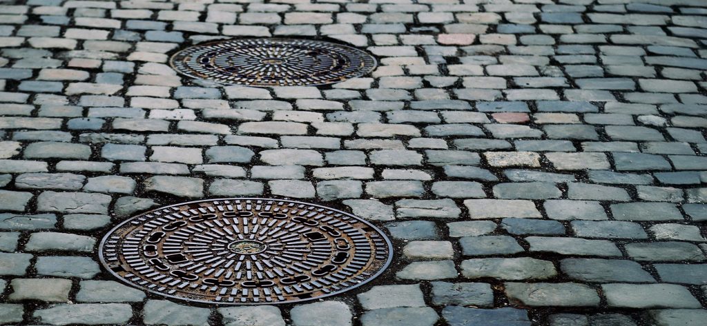 Kopfsteinpflaster mit zwei runden Gullydeckeln, die Teil eines Abscheidersystems sind