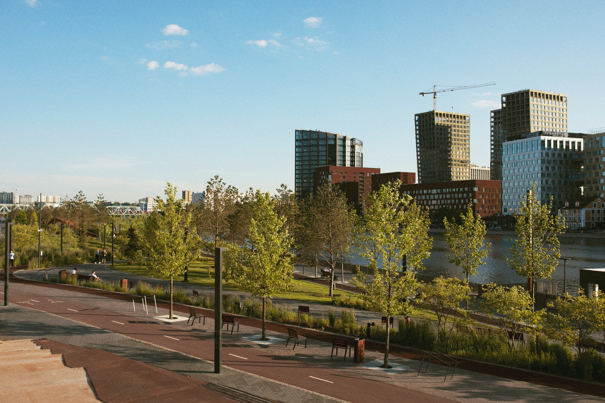 Städtische Uferpromenade mit Radweg, Bänken, Bäumen und modernen Hochhäusern im Hintergrund