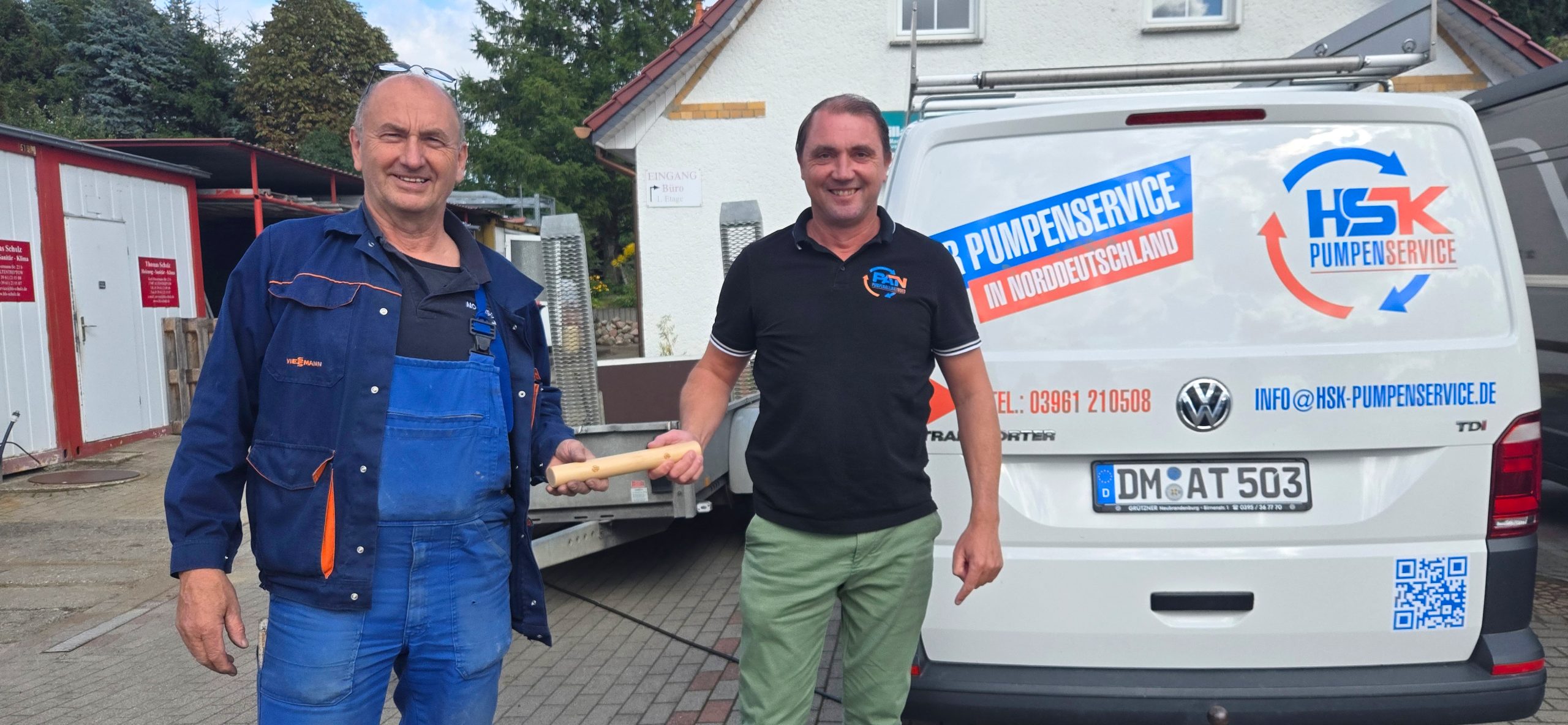 Zwei Männer stehen nebeneinander und übergeben einen Staffelstab, einer trägt blaue Arbeitskleidung, der andere ein schwarzes Poloshirt und grüne Hose, vor einem weißen Transporter mit HSK Pumpenservice-Logo.