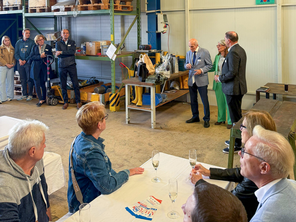 Mehrere Personen in einem Lagerraum hören bei einer Rede zu.