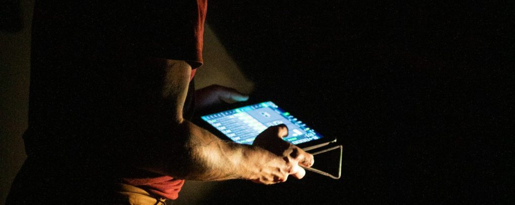 Mann steht in dunklem Raum, hält Tablet mit leuchtendem Bildschirm und bedient Pumpenauslegung.