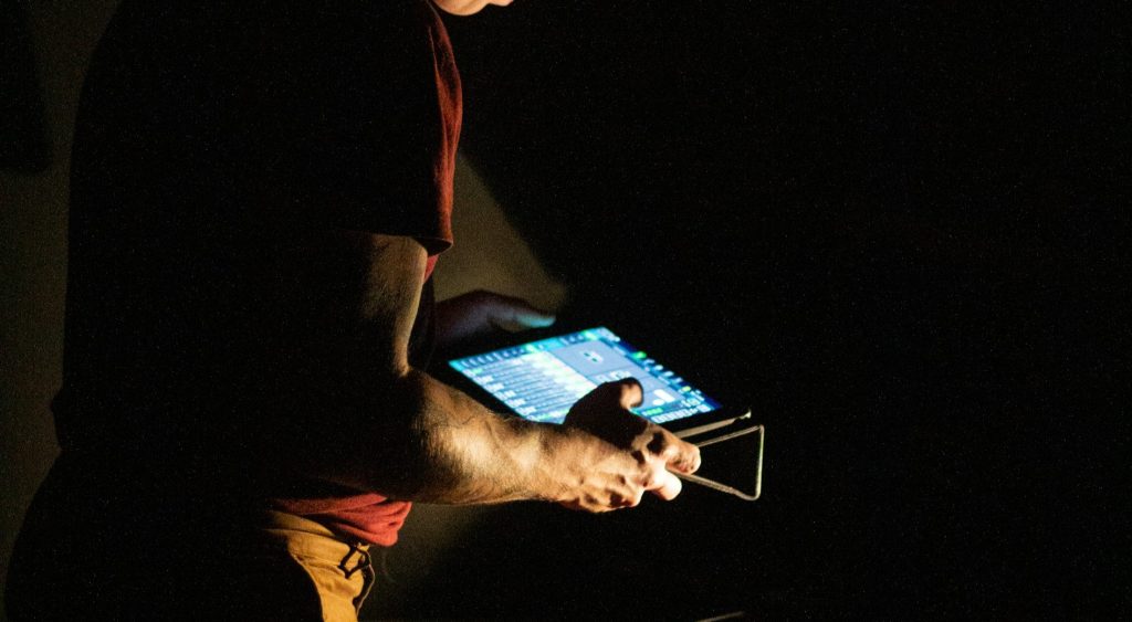 Person hält ein Tablet mit beleuchtetem Bildschirm in beiden Händen in dunkler Umgebung und kontrolliert die richtige Pumpenauslegung.