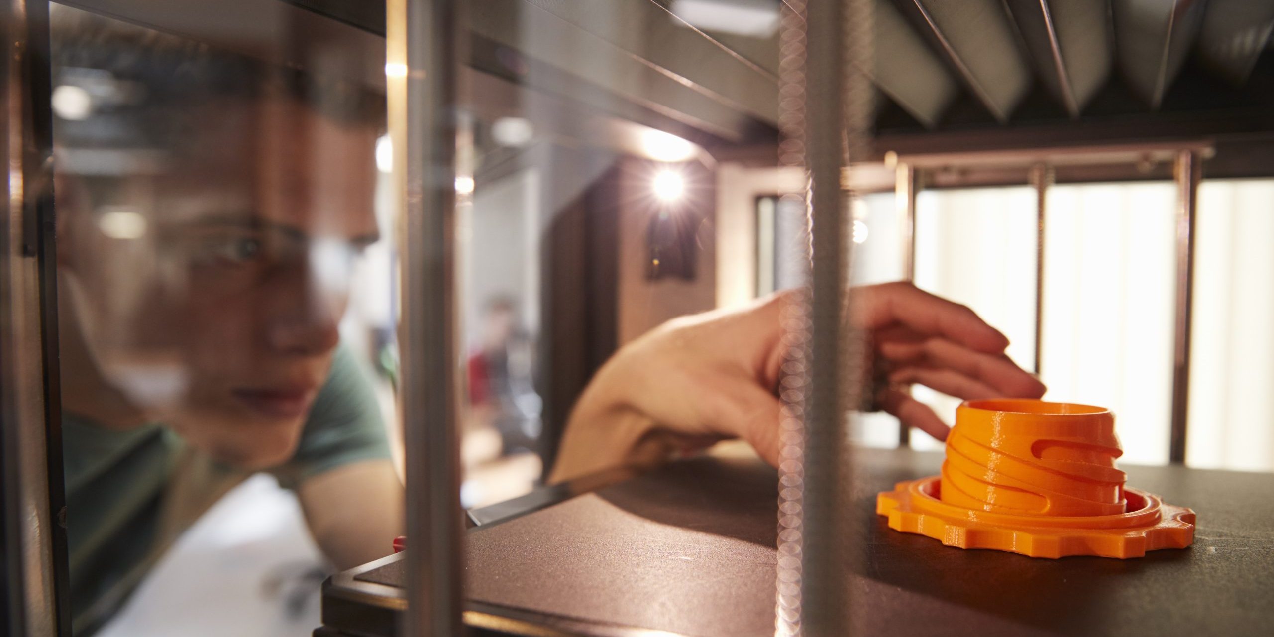 Hand eines Mannes, der ein orangefarbenes 3D-gedrucktes Objekt auf einer 3D-Druck Plattform berührt