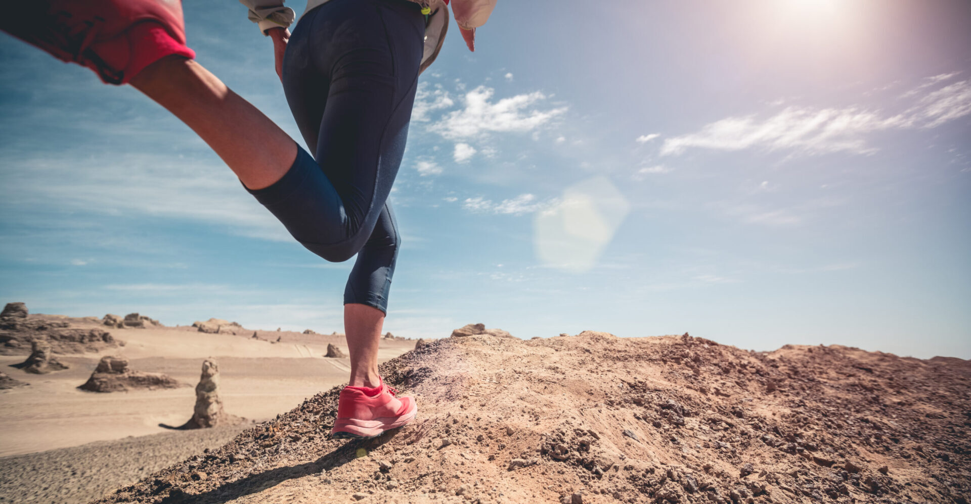 Frau mit Sportkleidung und roten Laufschuhen läuft über sandiges, trockenes Gelände. Trockenlauf