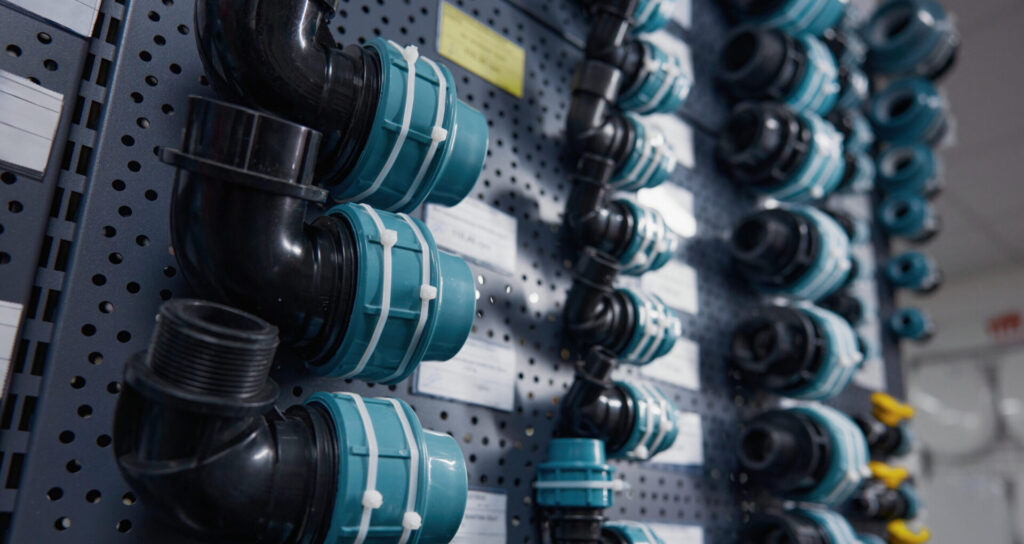 Mehrere schwarze Kunststoffadapter und PVC-Fittings mit blauen Manschetten sind an einer Lochwand befestigt.