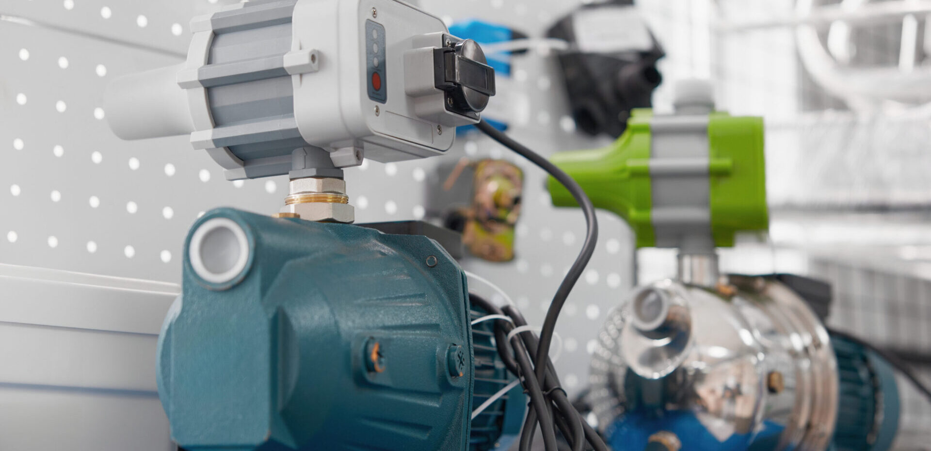 Zwei Pumpensteuerungen mit sichtbaren Kabeln und Gehäusen stehen nebeneinander vor einer Lochwand.