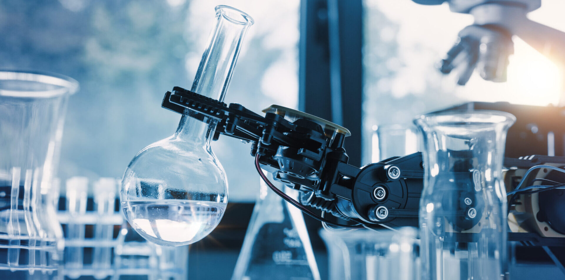 Ein Roboterarm hält einen Kolben zwischen mehreren Chemikalienpumpen und Laborgefäßen.