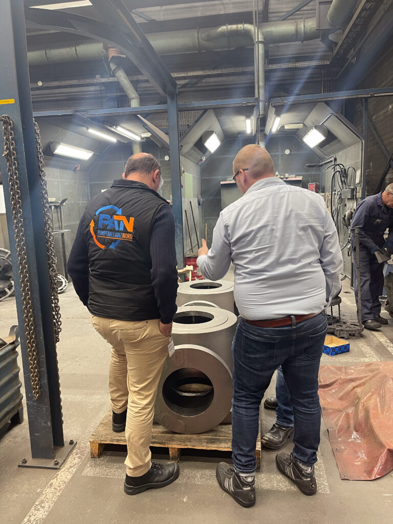 Zwei Männer stehen in einer Werkhalle neben drei großen zylindrischen Bauteilen von Pentair und unterhalten sich.