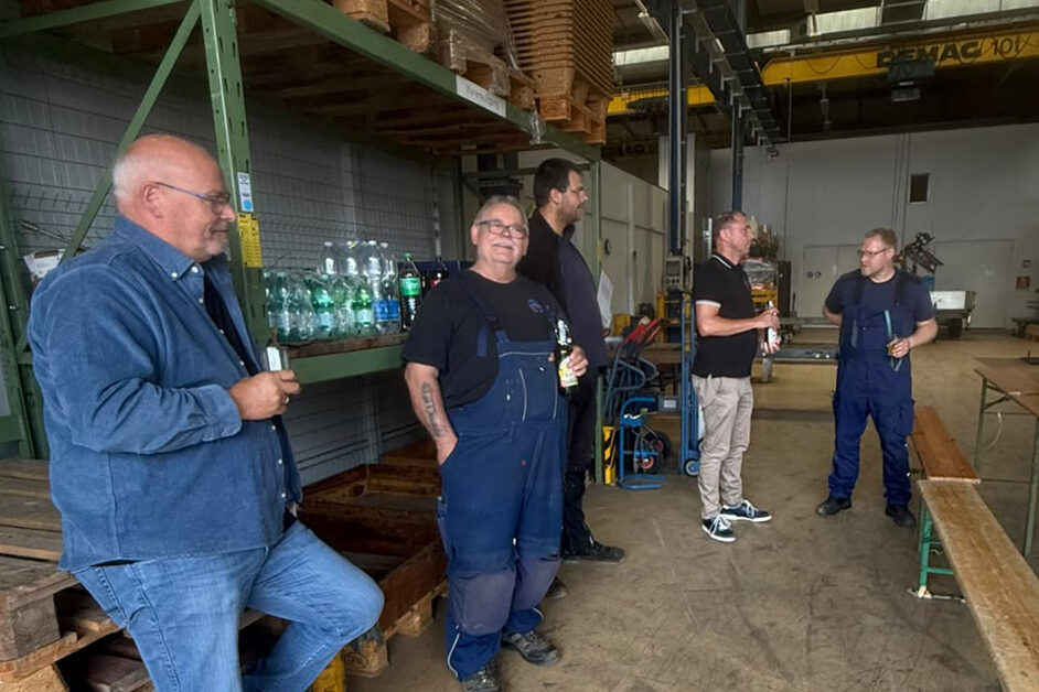 Mehrere Männer stehen in einer Lagerhalle neben Paletten und Getränkekisten und unterhalten sich.