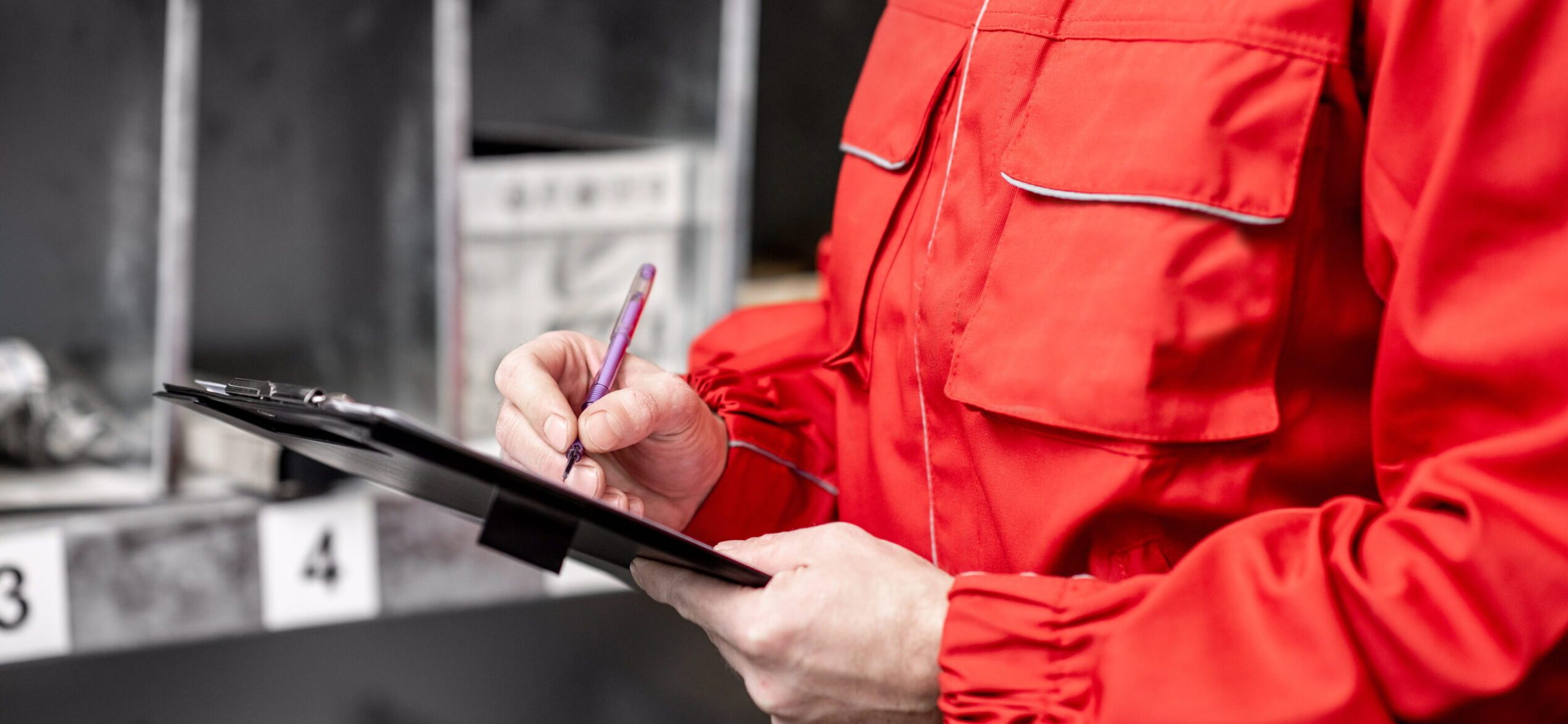 Arbeiter in roter Uniform schreibt etwas über die Pumpen Lebensdauer auf einen Wartungsplan.