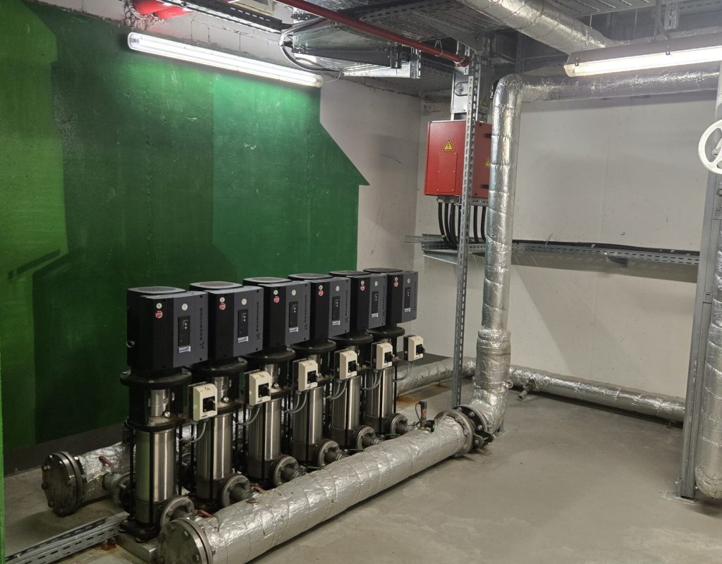 Druckerhöhungsanlage mit sechs vertikalen Pumpen und isolierten Rohrleitungen in einem Technikraum zur Trinkwasserversorgung